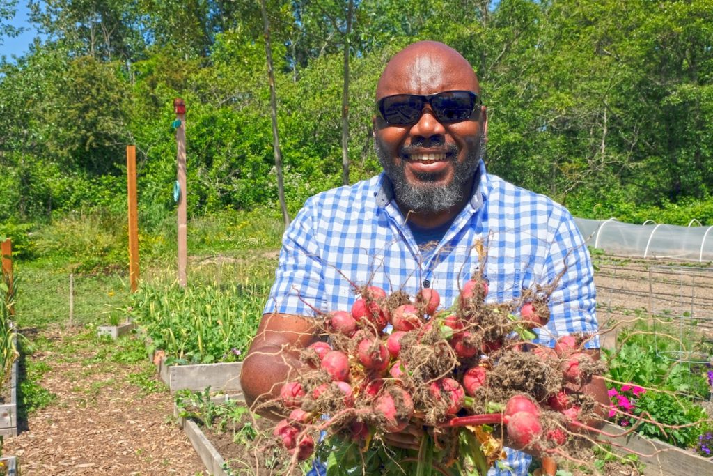 David Bulindah stands in a garden holding radishes