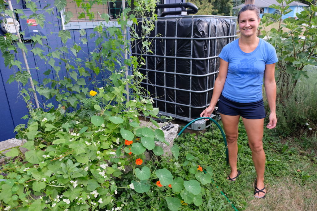 Laura holds a watering hose in front of a large rainwater collector